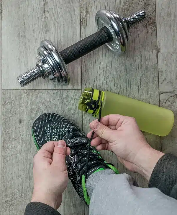 kädet solmivat urheilukengän nauhoja kiinni käsipainon ja vesipullon vieressä